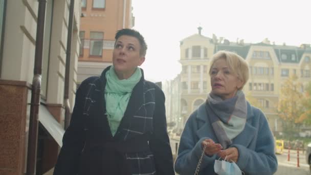 Две женщины среднего возраста надевают защитные маски на улице — стоковое видео
