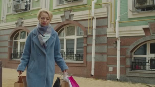 Leeftijd vrouw met veel papieren tassen vangen taxi tijdens het winkelen in de stad — Stockvideo