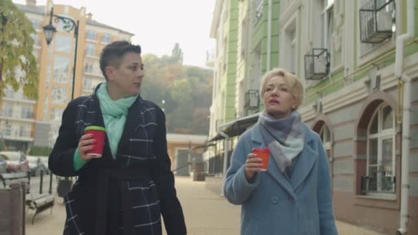 Två mogna kvinnor dricker kaffe i engångskoppar utomhus — Stockvideo
