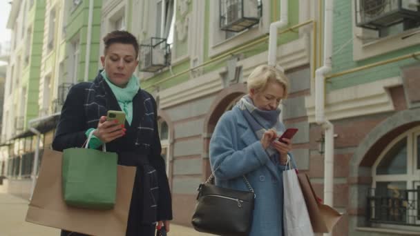 Dos mujeres maduras obsesionadas con los teléfonos durante las compras de ocio al aire libre — Vídeos de Stock