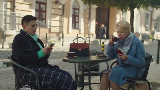 Mulheres de negócios maduras sentadas à mesa do café, usando smartphone ao ar livre — Vídeo de Stock