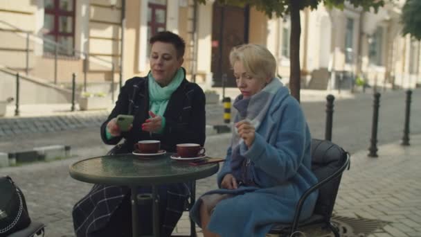 Oudere vrouwelijke paar nemen selfie zitten aan cafe tafel buiten — Stockvideo