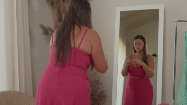 Plump woman in pink dress putting on lipstick in front mirror indoors — Stock Video