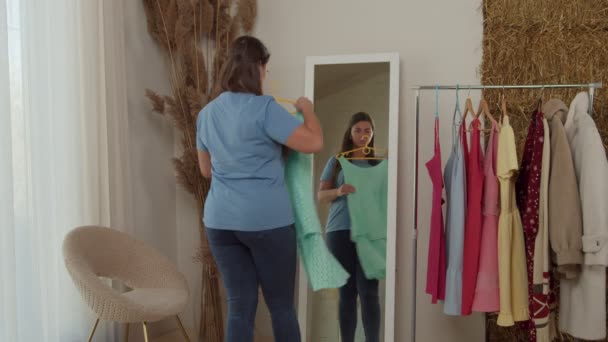 Mujer adulta regordeta tratando de vestidos en pie en el espejo delantero en interiores — Vídeo de stock