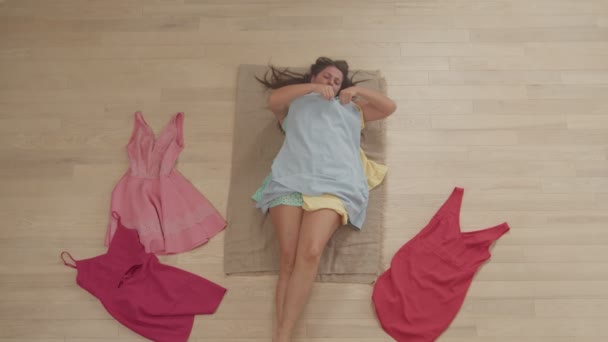 Top vinkel syn på fyllig kvinna att välja klänningar liggande på golvet inomhus — Stockvideo
