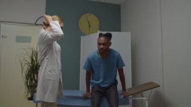 Kadın doktor, içeride steteskop kullanan genç bir erkek hastayı muayene ediyor.