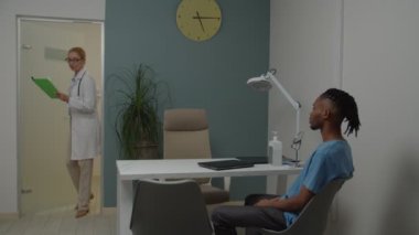 Genç yetişkin hasta doktor muayenehanesinde kadın doktoru selamlıyor.