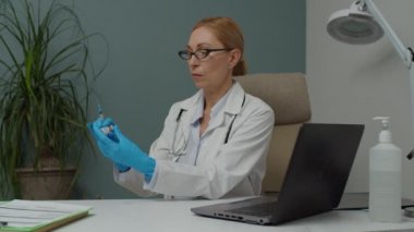 Koruyucu eldivenli kadın doktor şırıngayı kapalı alanda aşıyla dolduruyor.