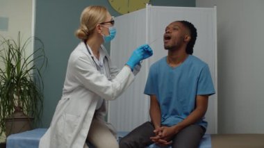 Kadın doktor, içeride boğaz ağrısı var mı diye genç adamı kontrol ediyor.