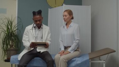 Doktor, kadın hastaya içeride tablet kullanarak teşhisi açıklıyor.