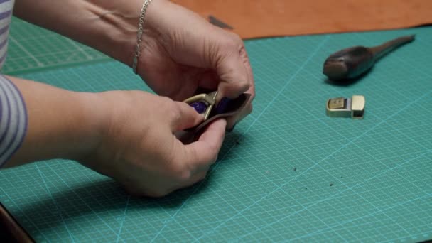 Κοντινό πλάνο χέρια γυναίκα εισάγοντας μεταλλικό υλικό σε δερμάτινο κομμάτι σε εσωτερικούς χώρους — Αρχείο Βίντεο