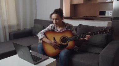 Kadın içeride dizüstü bilgisayar dersleri alarak gitar çalmayı öğreniyor.