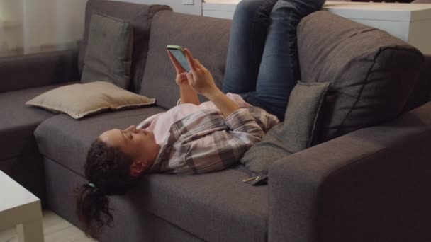 ソファの上にインターネット経由でモバイルアプリを使用して女性のオンラインメッセージング、屋内 — ストック動画