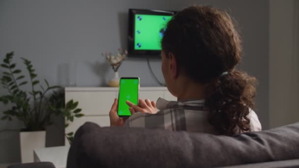 Камера бокового обзора, женщина, использующая удаленное мобильное приложение для телевизора, экран хромакея — стоковое видео