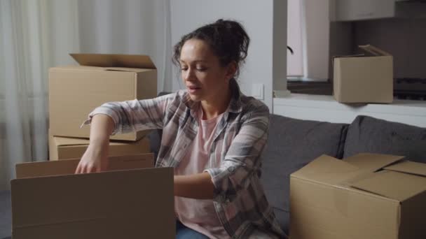 Positive adult woman unpacking cardboard box while moving new home