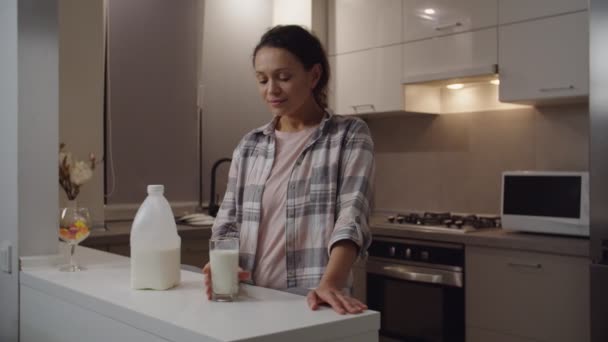 Доросла жінка приймає ковток молока, насолоджуючись свіжістю молока в приміщенні — стокове відео