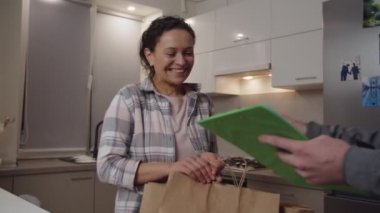 Neşeli, yetişkin bir kadın, içinde ürünler olan paket paketleri alıyor.