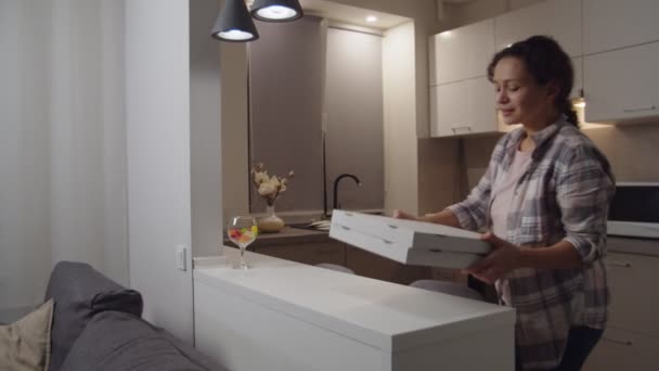 Volwassen vrouw die de doos opent, pizza ruikt, glimlacht in de keuken — Stockvideo