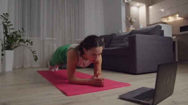 女性でスポーツウェアのパフォーマンスヒップディップワークアウトを使用してノートパソコンで自宅 — ストック動画