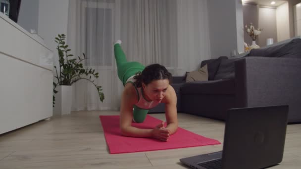 Mulher em sportswear executando perna alongamento exercício laptop dentro de casa — Vídeo de Stock