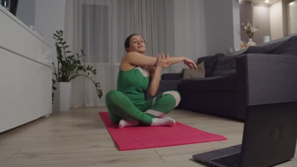 Mujer adulta calentando, viendo video tutorial en el ordenador portátil en casa — Vídeo de stock