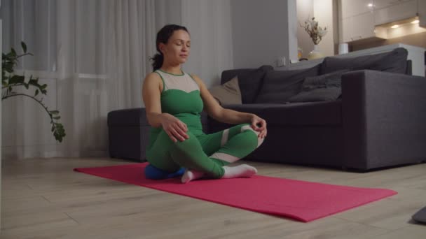 Spor kıyafetli yetişkin bir kadın açık dizüstü bilgisayarın önünde meditasyon yapıyor. — Stok video