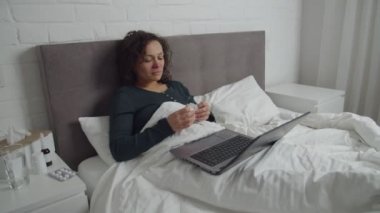 Hasta yetişkin kadın yatakta uzanıyor, video seyrediyor, dizüstü bilgisayarda film izliyor.