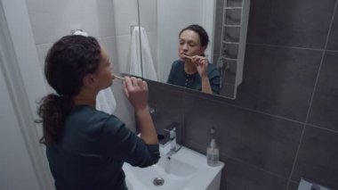 Siyah kadın dişlerini fırçalıyor, dans ediyor, banyoda aynanın önünde dikiliyor.