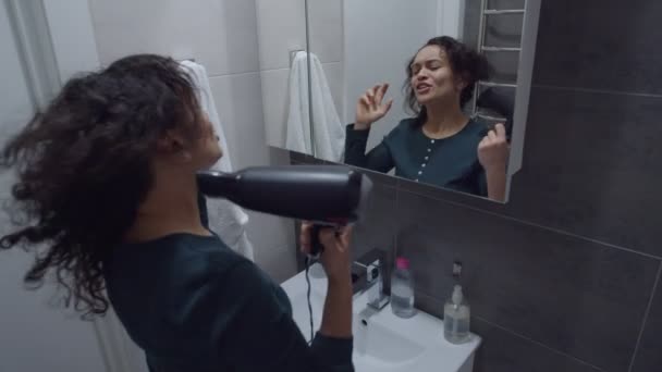 Όμορφη μαύρη γυναίκα αισθάνεται ευτυχισμένη, τραγουδώντας, χρησιμοποιώντας στεγνωτήρα μαλλιών σε εσωτερικούς χώρους — Αρχείο Βίντεο