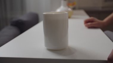 Tanımlanamayan bir kadın eli, beyaz bardağı kapalı alandan alıyor.