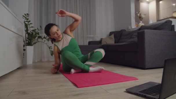 Sporty woman doing stretching workout, looking at laptop indoors — ストック動画