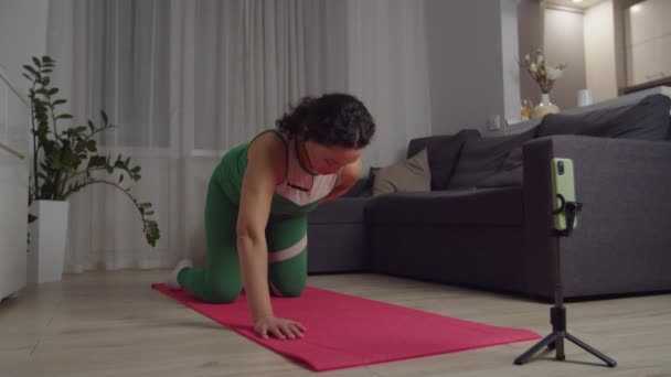 Mulher adulta desportiva segurando treino distante, usando smartphone em casa — Vídeo de Stock