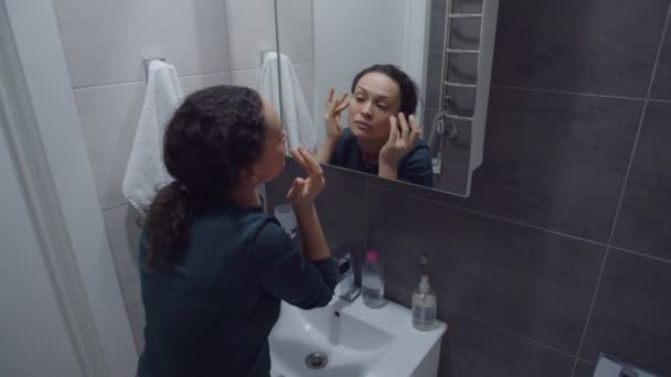 Urocza dorosła kobieta sprawdza skórę twarzy pod kątem zmarszczek i trądziku w pomieszczeniach — Wideo stockowe