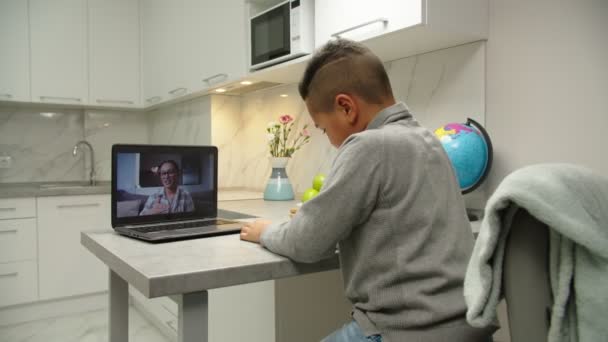 Profesora sosteniendo videollamada con el niño de la escuela usando portátil en interiores — Vídeo de stock