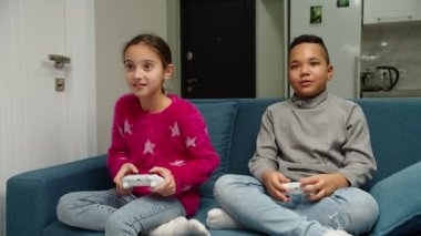 Çok ırklı erkek ve kız video oyunu oynuyor, kanepede oturuyor.