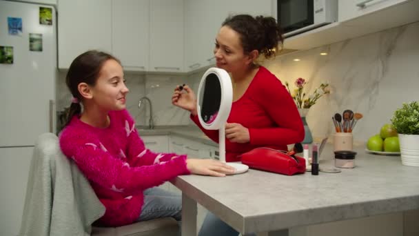 Щаслива дівчина, дивлячись на дзеркало марнославства, перевіряє макіяж в приміщенні — стокове відео