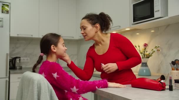 Caring mother teaching daughter putting on makeup on face skin indoors — Stock Video