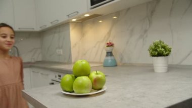 Meyve alan küçük kız, elma ısıran, kapalı alanda gülümseyen.