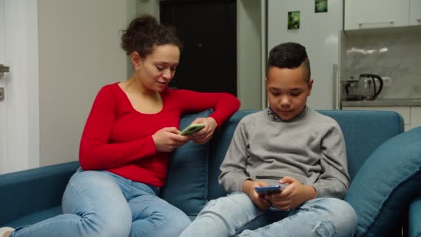 Madre y su hijo preadolescente usando un teléfono inteligente, navegando por la red en el interior — Vídeo de stock