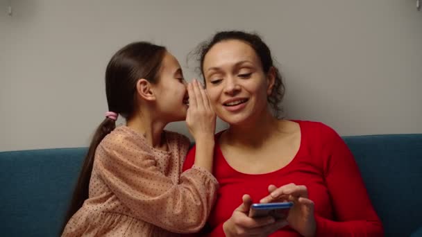 Милая дочь рассказывает секрет улыбающейся многонациональной матери дома — стоковое видео