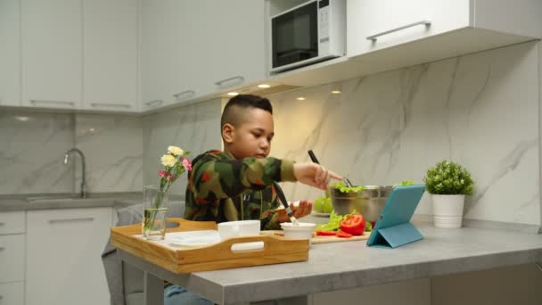 Chico guapo siguiendo receta de cocina, utilizando tableta digital en el interior — Vídeos de Stock