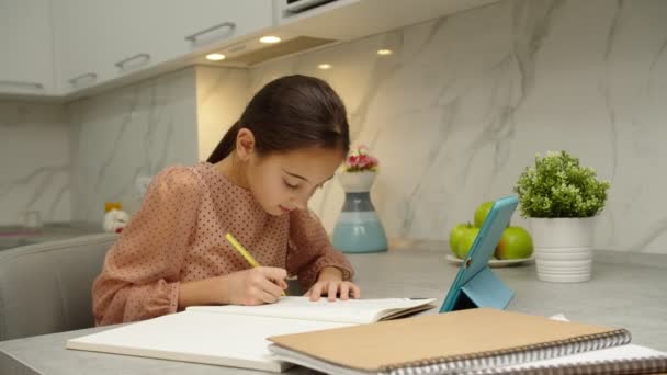 Estudante escrevendo em copybook, levantando a mão para responder ao tutor online — Vídeo de Stock