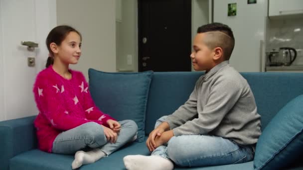 Багатоетнічні діти грають, жестикулюють, високі п'ять сидять на дивані в приміщенні — стокове відео