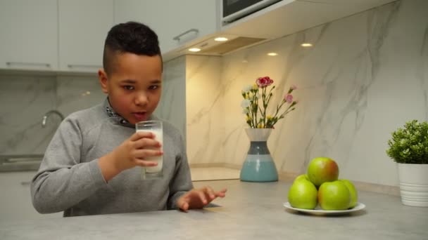 A gyerek tejet iszik, mosolyog, élvezi az ökológiai termék ízét otthon — Stock videók