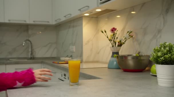 Сором'язлива дівчина в рожевому светрі бере склянку апельсинового соку вдома — стокове відео