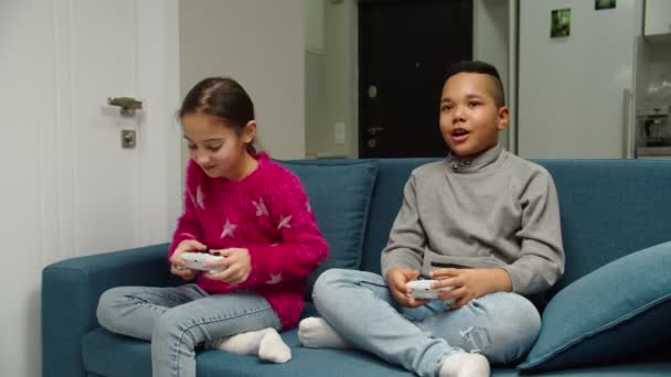 Movendo tiro de diversas crianças multiétnicas jogando videogame dentro de casa — Vídeo de Stock