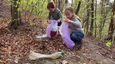 Güzel anaokulu kızı gülümsüyor, içi çöp dolu plastik torba gösteriyor. 