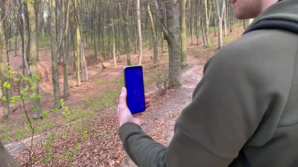 Камера відкриває вид ззаду молодого дорослого туриста-чоловіка зі смартфоном — стокове відео