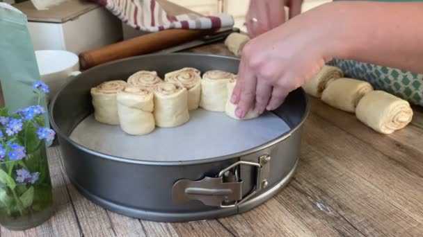 Женщина кладет булочки с корицей в выпечку на домашней кухне — стоковое видео