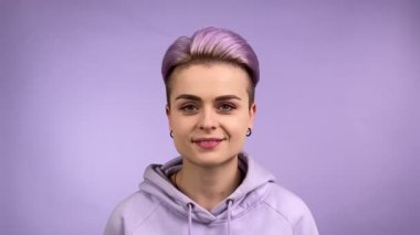 Mutlu gülümseyen, stil sahibi, havalı, genç, yetişkin bir kadın, kısa saçlı, mor arka planda izole edilmiş kameraya bakan, modaya uygun, mor saçlı bir kadın. Vesikalık portreyi kapat.